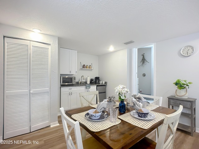 dining space with baseboards, visible vents, light wood-type flooring, and a textured ceiling