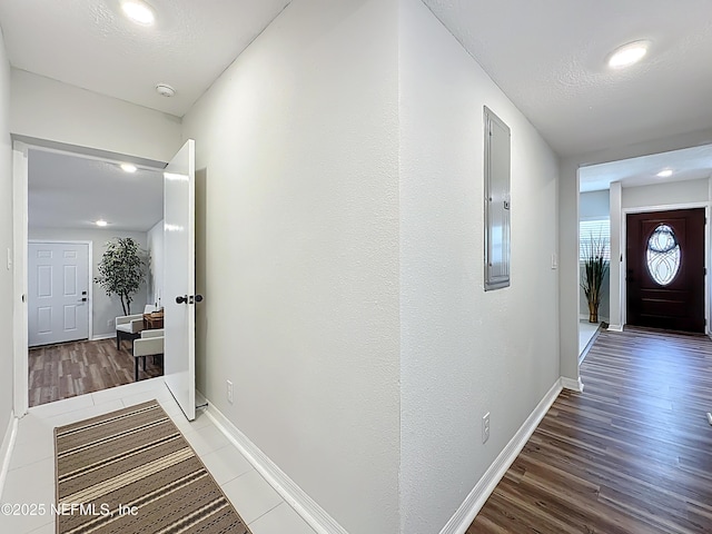 corridor featuring baseboards, recessed lighting, wood finished floors, and electric panel