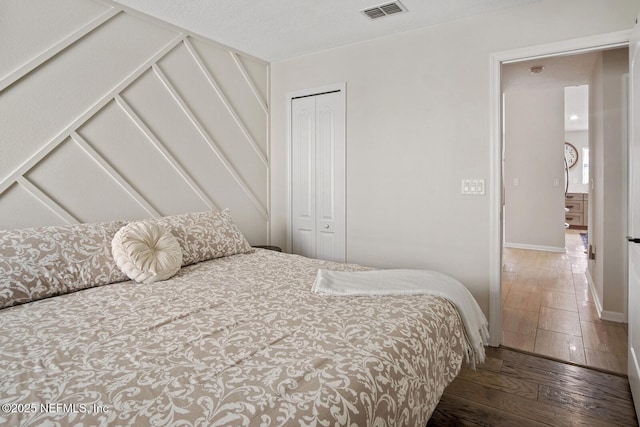 bedroom featuring baseboards, visible vents, hardwood / wood-style flooring, and a closet