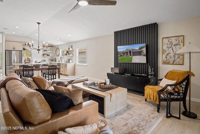 living room featuring a textured ceiling, vaulted ceiling, baseboards, ceiling fan with notable chandelier, and light wood-style flooring