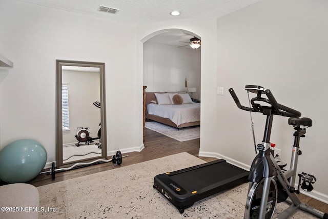 exercise area featuring arched walkways, baseboards, visible vents, and wood finished floors