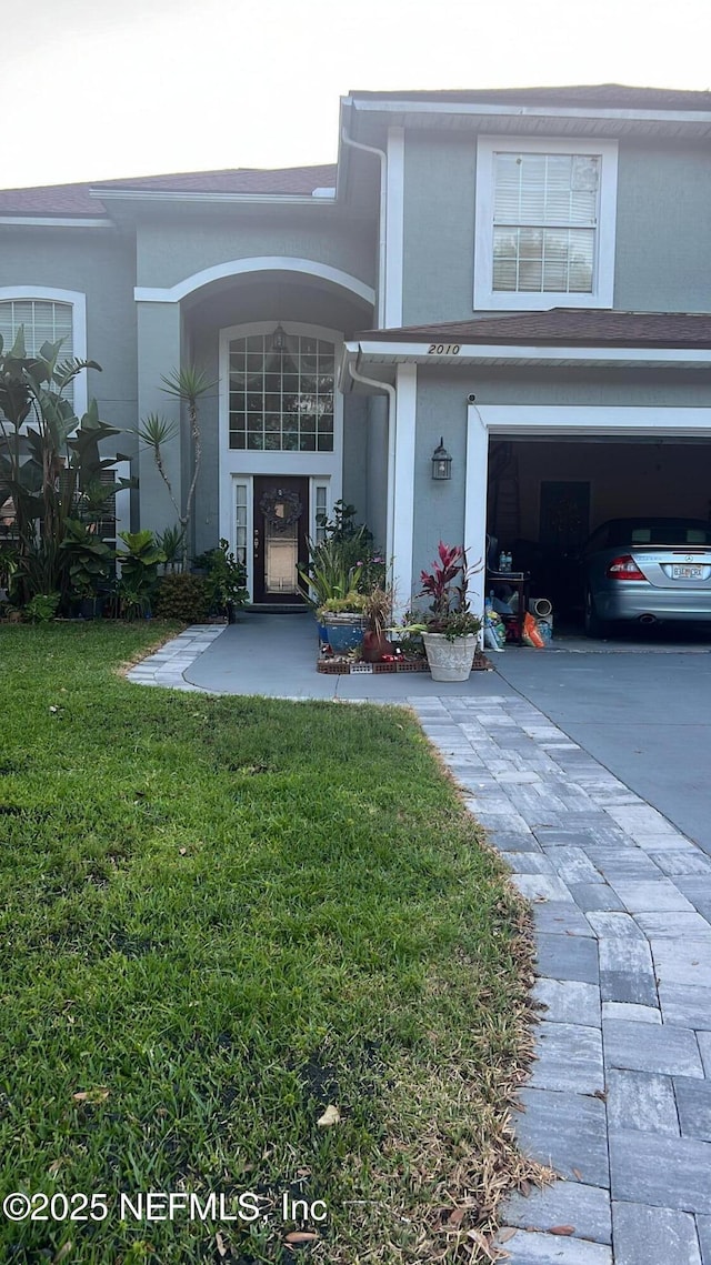 view of exterior entry featuring a lawn, driveway, stucco siding, and a garage