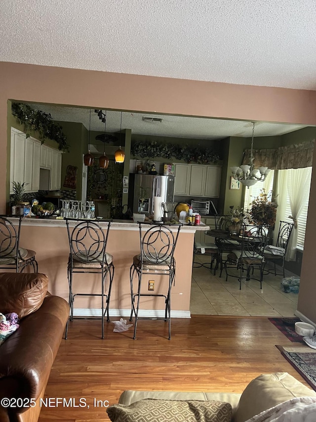 living room featuring a textured ceiling, visible vents, a toaster, light wood finished floors, and a chandelier