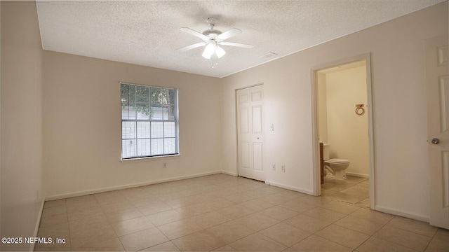 unfurnished bedroom featuring a textured ceiling, light tile patterned floors, visible vents, ensuite bathroom, and baseboards