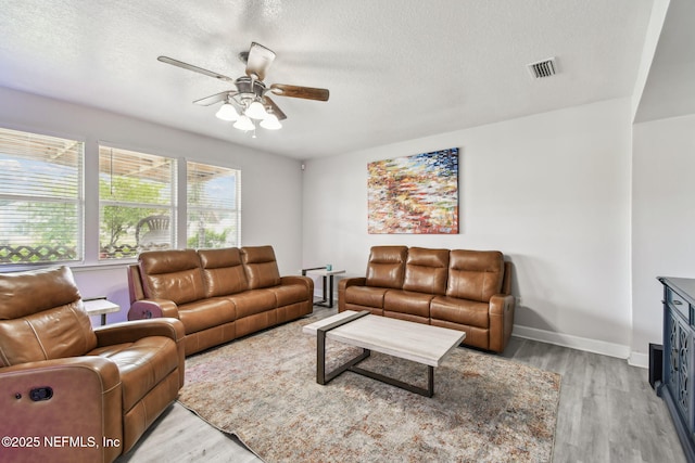 living room with a textured ceiling, visible vents, ceiling fan, and light wood-style flooring