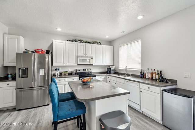 kitchen featuring a sink, stainless steel appliances, light wood-type flooring, dark countertops, and a textured ceiling