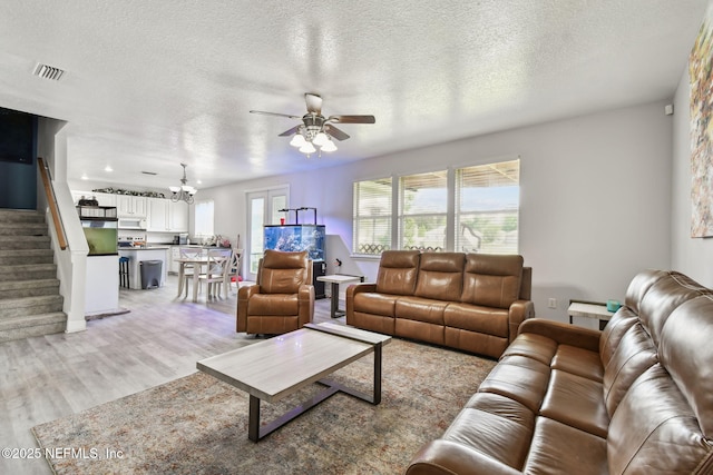 living area with stairs, light wood-style floors, ceiling fan with notable chandelier, visible vents, and a textured ceiling