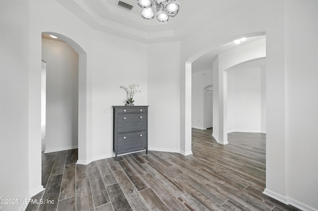 interior space with arched walkways, dark wood-style floors, visible vents, a raised ceiling, and a notable chandelier