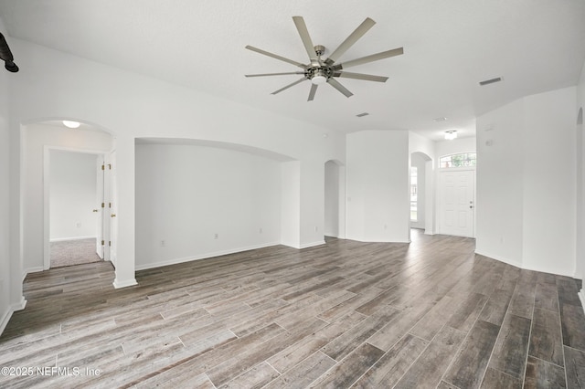 unfurnished living room with wood finished floors, ceiling fan, and arched walkways