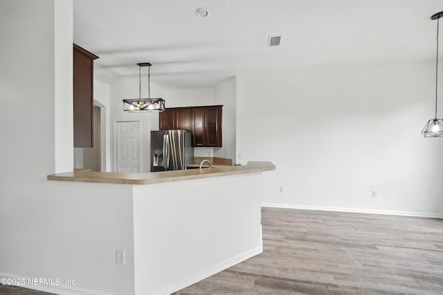 kitchen featuring arched walkways, hanging light fixtures, light wood-style floors, stainless steel fridge with ice dispenser, and visible vents