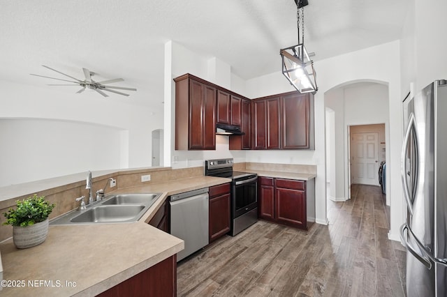 kitchen featuring arched walkways, stainless steel appliances, under cabinet range hood, a sink, and a ceiling fan