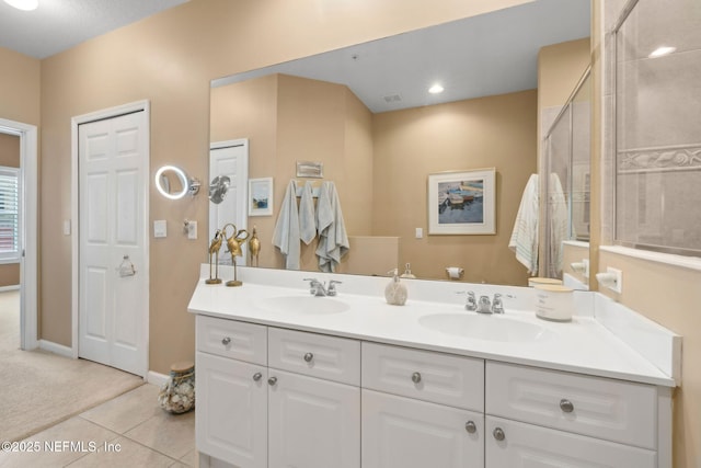 bathroom with tiled shower, tile patterned flooring, double vanity, and a sink