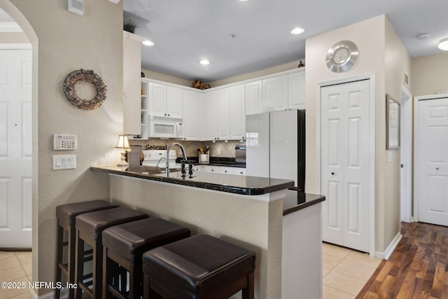 kitchen with arched walkways, white appliances, open shelves, dark countertops, and a peninsula