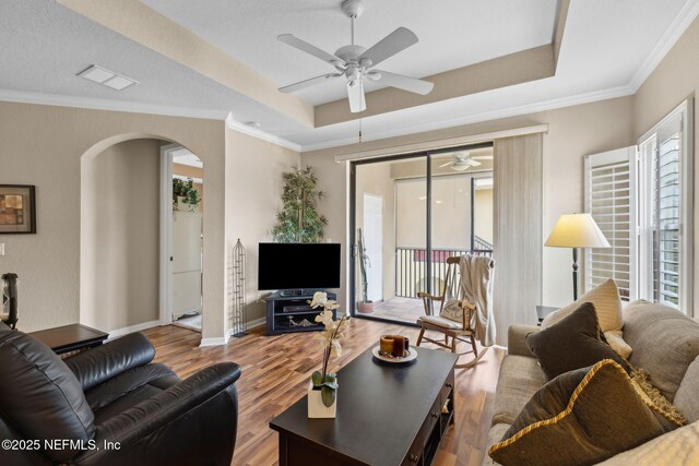 living room featuring a wealth of natural light, a raised ceiling, ceiling fan, and arched walkways
