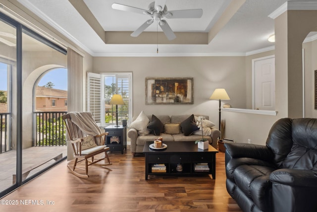 living room with wood finished floors, arched walkways, ceiling fan, a raised ceiling, and crown molding