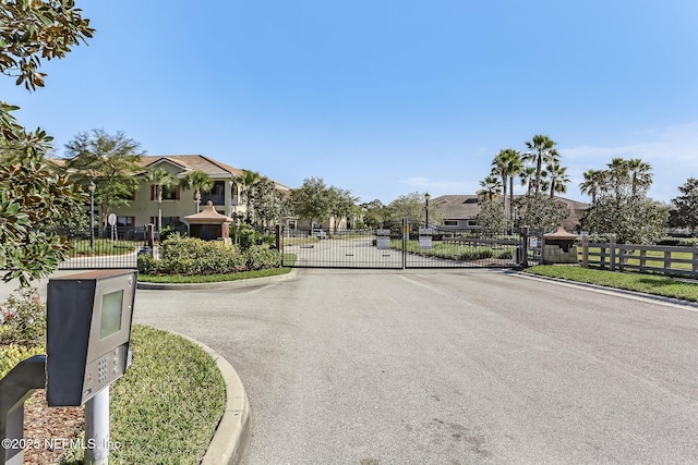 view of road featuring a gate, curbs, a residential view, and a gated entry