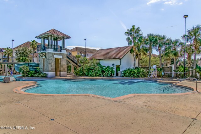 pool with stairway, a water slide, and a patio area