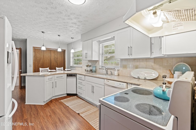 kitchen with a sink, white cabinetry, a peninsula, white appliances, and wood finished floors