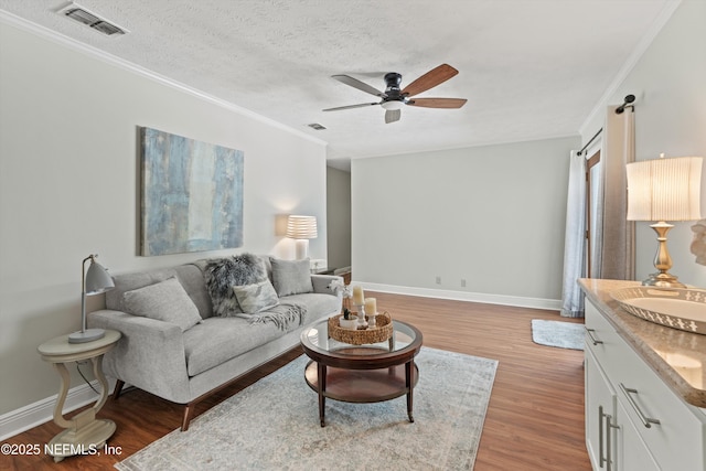 living area with ornamental molding, a ceiling fan, light wood-style flooring, and baseboards