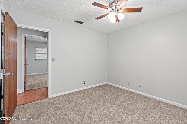 spare room with ceiling fan, visible vents, baseboards, a textured ceiling, and carpet floors