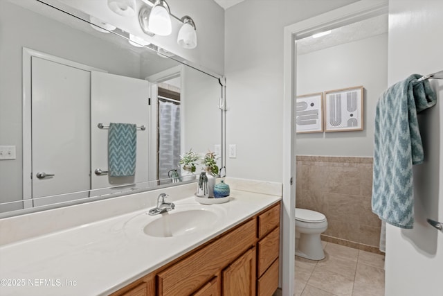 bathroom with tile walls, vanity, toilet, a wainscoted wall, and tile patterned flooring