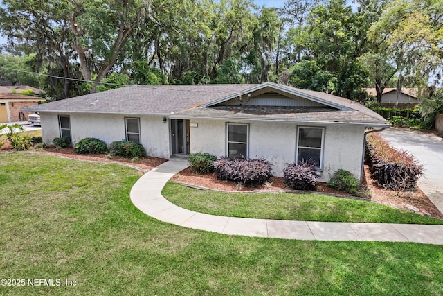 single story home with a front lawn, a shingled roof, and stucco siding