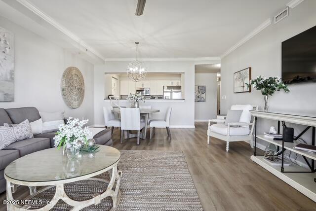 living area with a chandelier, wood finished floors, ornamental molding, and baseboards