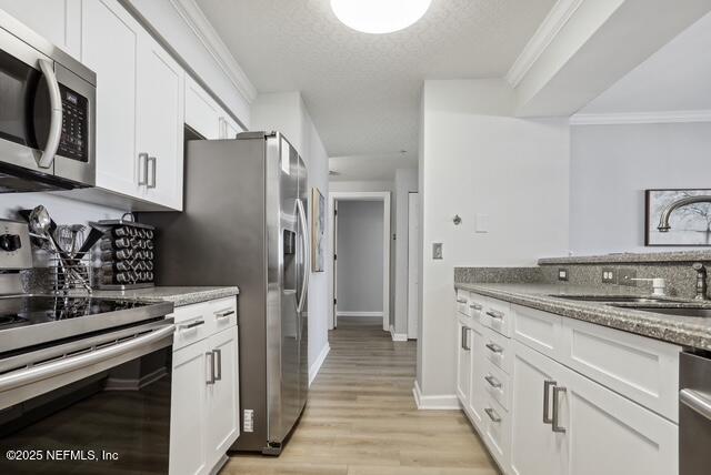 kitchen featuring stainless steel appliances, white cabinets, stone counters, light wood-style flooring, and a textured ceiling