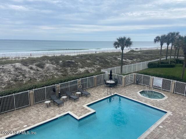 community pool featuring a hot tub, fence, view of water and beach, and a patio area