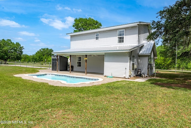 rear view of property with a fenced in pool, a fenced backyard, metal roof, and a lawn
