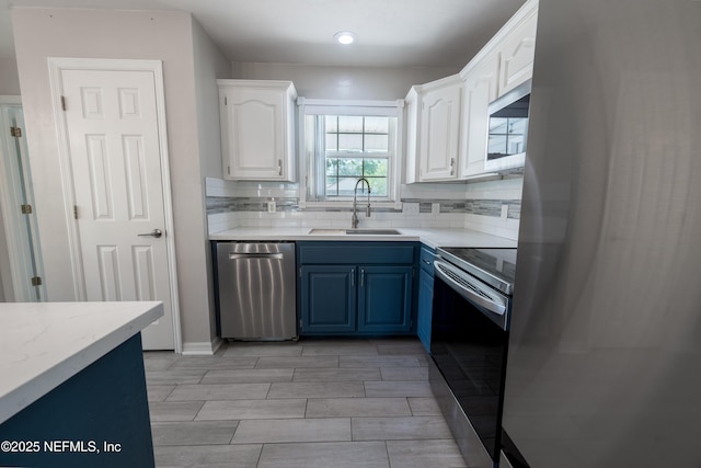 kitchen featuring tasteful backsplash, blue cabinets, stainless steel appliances, white cabinets, and a sink