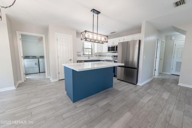 kitchen with appliances with stainless steel finishes, light countertops, light wood-type flooring, washing machine and dryer, and visible vents
