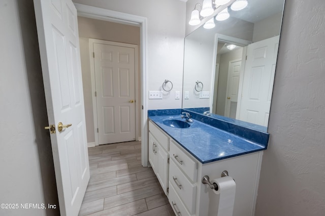 bathroom featuring wood finished floors, a notable chandelier, a textured wall, and vanity