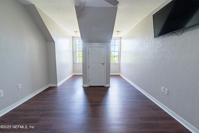 additional living space featuring dark wood-type flooring, a textured wall, a ceiling fan, and baseboards