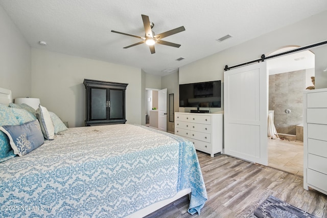bedroom with visible vents, a barn door, a ceiling fan, and wood finished floors