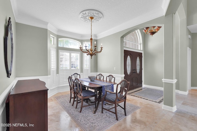 dining room with crown molding, wainscoting, a decorative wall, a textured ceiling, and a chandelier