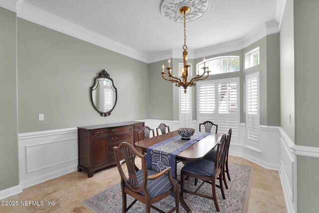 dining space featuring crown molding, wainscoting, a decorative wall, and a chandelier