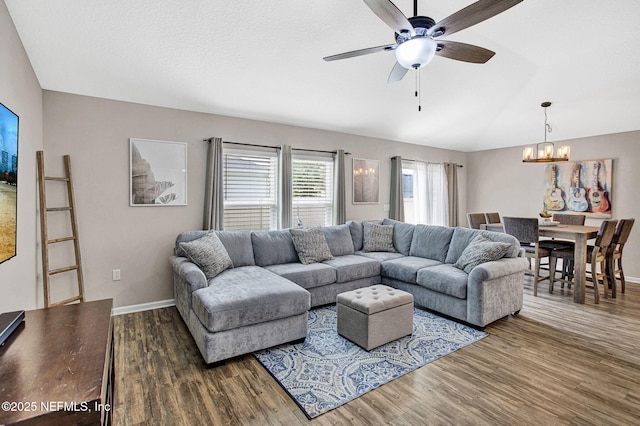 living area featuring vaulted ceiling, baseboards, ceiling fan with notable chandelier, and wood finished floors