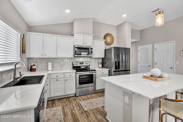 kitchen featuring white cabinets, appliances with stainless steel finishes, a sink, wood finished floors, and backsplash