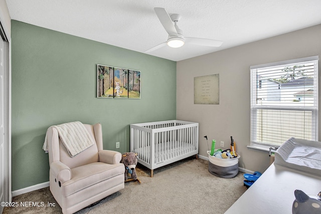 carpeted bedroom featuring ceiling fan, a crib, and baseboards