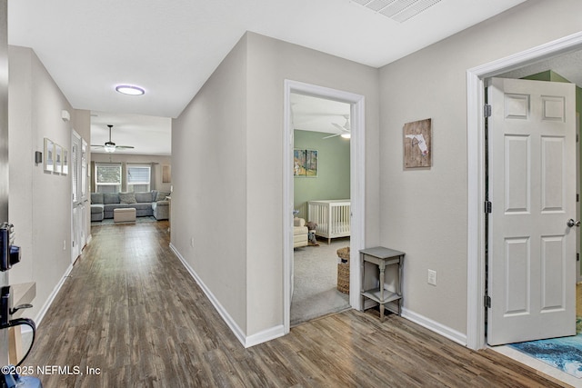 corridor with baseboards, wood finished floors, and visible vents