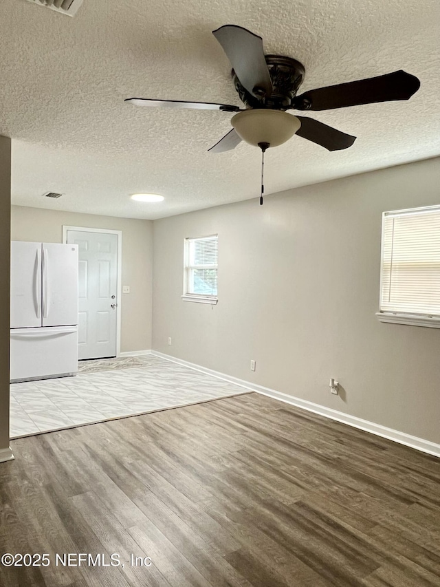 empty room featuring ceiling fan, a textured ceiling, baseboards, and wood finished floors