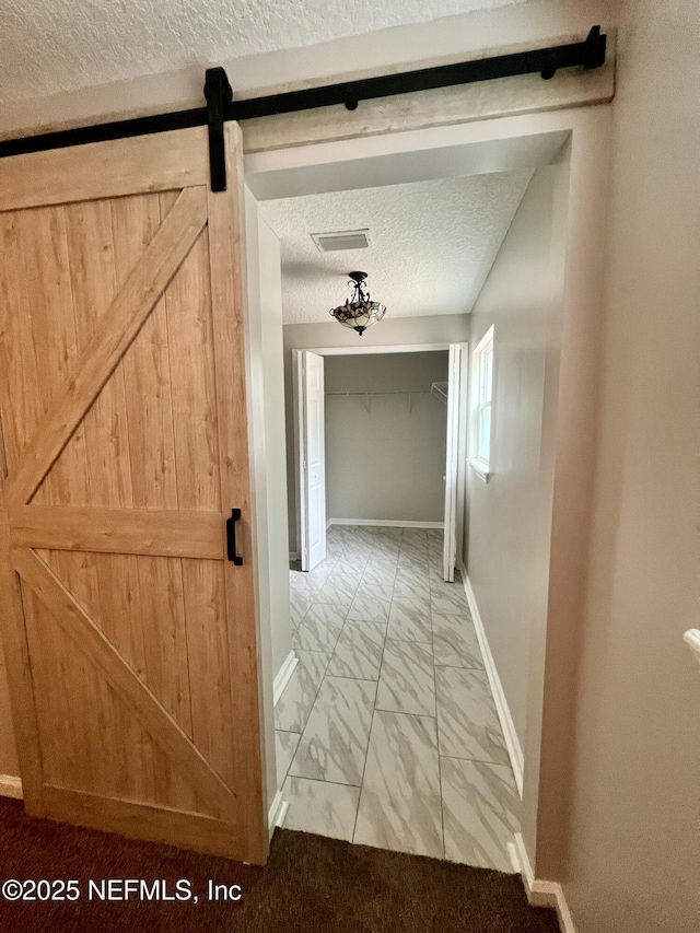 hall featuring a textured ceiling, visible vents, a barn door, baseboards, and marble finish floor