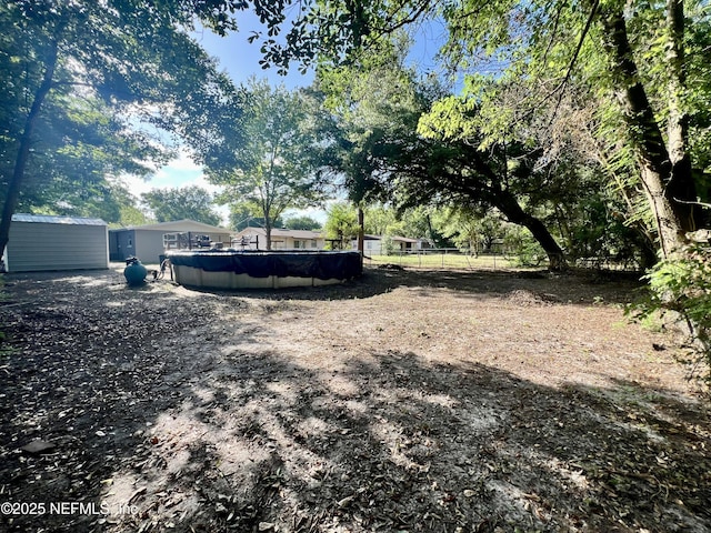 view of yard featuring a storage shed, fence, a fenced in pool, and an outbuilding