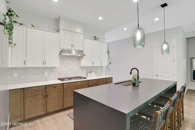 kitchen featuring stainless steel gas stovetop, under cabinet range hood, backsplash, a kitchen bar, and a sink