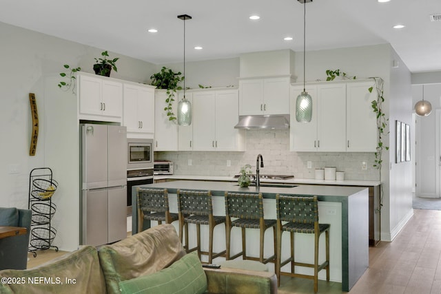kitchen with a sink, stainless steel appliances, backsplash, and under cabinet range hood