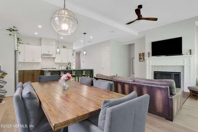 dining room with a brick fireplace, recessed lighting, a ceiling fan, and light wood-type flooring