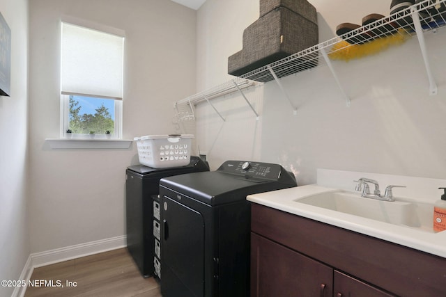 laundry area with wood finished floors, independent washer and dryer, cabinet space, a sink, and baseboards