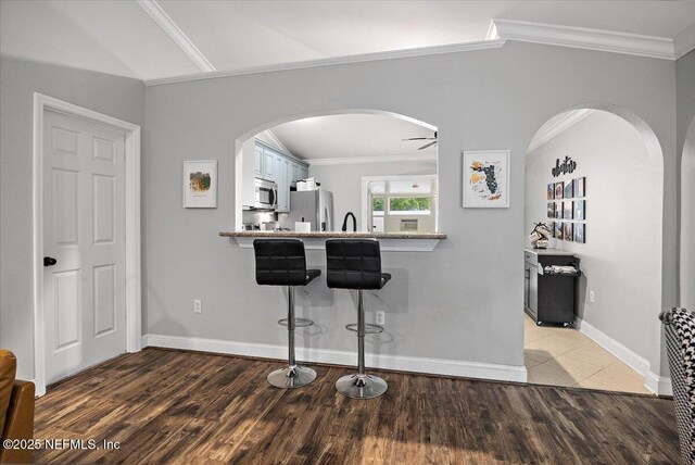 2681 Kimberly Forest Dr E, Jacksonville, FL 32246 - kitchen featuring appliances with stainless steel finishes, arched walkways, ornamental molding, a kitchen bar, and light wood-type flooring