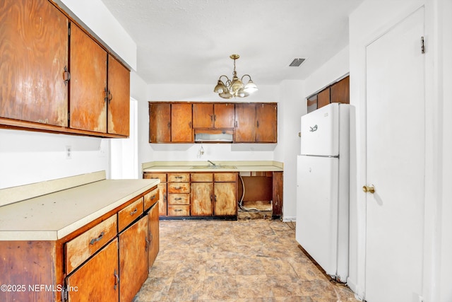 kitchen with brown cabinets, a sink, light countertops, freestanding refrigerator, and an inviting chandelier